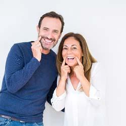 man and woman with dental implants in Pearland pointing to their smiles