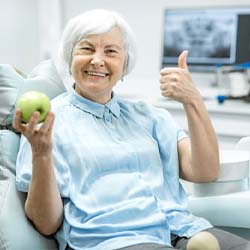senior woman holding an apple in the dental chair