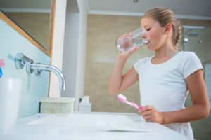 girl drinking water with toothbrush in bathroom 