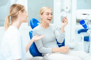 a woman smiling at her new teeth with her dentist