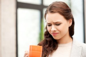 young woman with brown hair in a tan sweater looking down in disgust at her orange mug